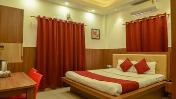 A hotel room with a wooden bed, red curtains, a wooden desk, and a coffee pot.