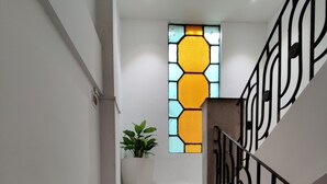 A staircase with a geometric railing, a potted plant, and a stained glass window in the background. - Magnolia Inn near GNRC & Secretariat, GS Rd (Guwahati)