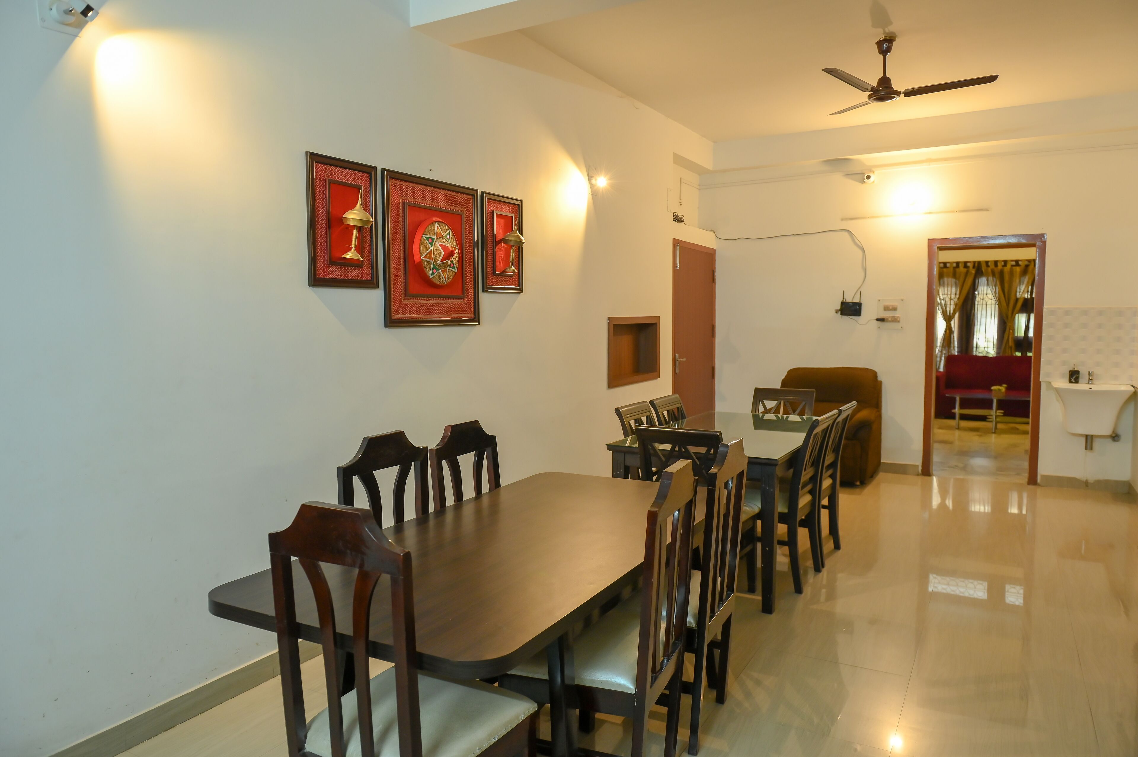 A dining area with a long wooden table, multiple chairs, and framed artwork on the wall.