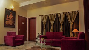 A hotel lobby with a red sofa, a glass coffee table, a red armchair, a painting on the wall, and a curtain with a tassel. - Magnolia Inn near GNRC & Secretariat, GS Rd (Guwahati)
