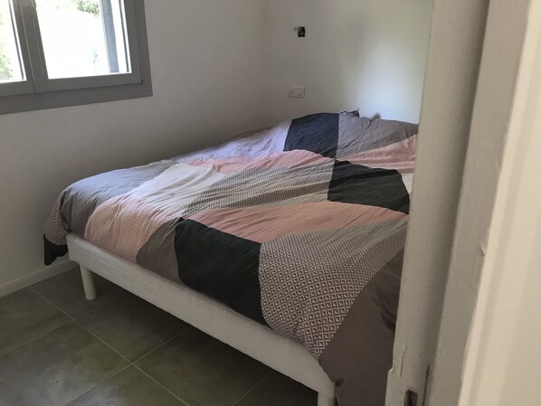 A single bed with a patterned bedspread in a room with a tiled floor and a window.