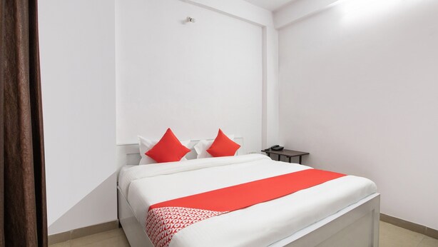 Una cama bien hecha con colcha blanca y roja, dos almohadas rojas y una mesita de noche con lámpara.