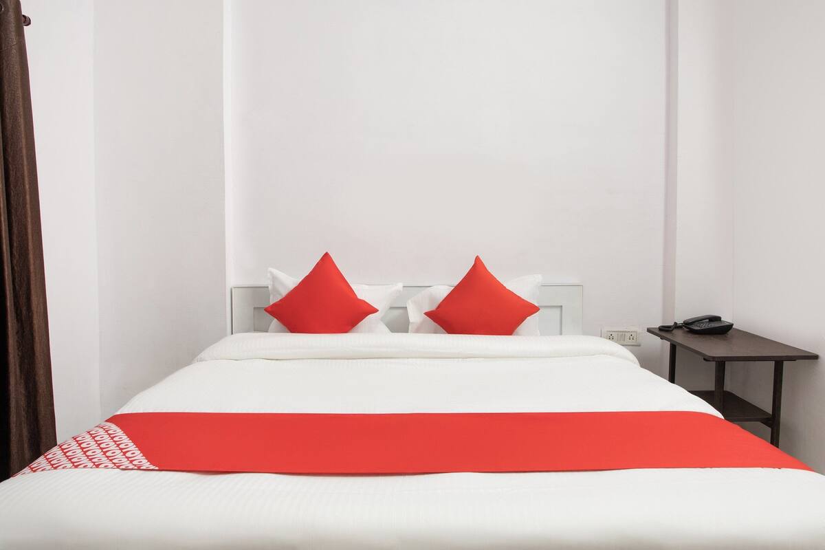 Una camera d'albergo con un letto, due cuscini rossi, un copripiumino bianco e una coperta rossa.