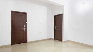 Una habitación con dos puertas cerradas, paredes blancas y suelo de baldosas.
