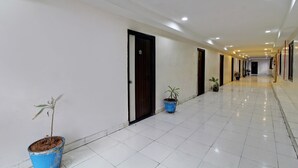 A clean, well-lit hallway with white tiled floors and doors, leading to rooms. There are potted plants placed along the hallway. - OYO 43619 Sahasra Residency (Hyderabad)