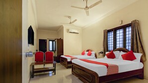 A hotel room with two single beds, a dining table, red chairs, a ceiling fan, and an air conditioning unit. - OYO 43619 Sahasra Residency (Hyderabad)