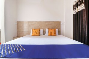 A hotel room with a bed, two pillows with a pattern, a blue blanket, and a window with curtains. - OYO 43300 Spring Woods Suites (Mohali)