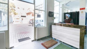 A reception area with a receptionist, a reception desk, a large window, and a view of the street outside. - OYO 43300 Spring Woods Suites (Mohali)