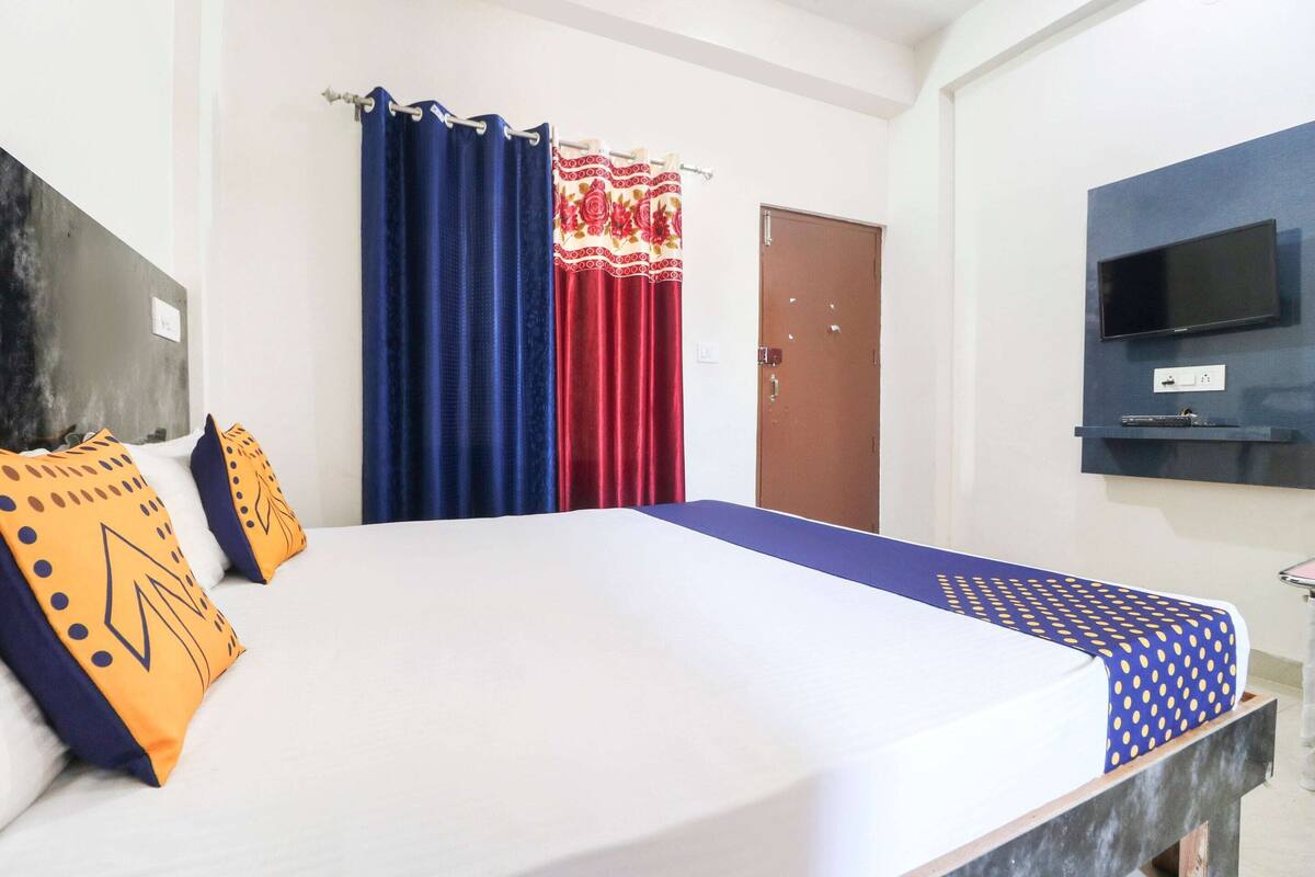 A hotel room with a bed, curtains, a television, and a door.