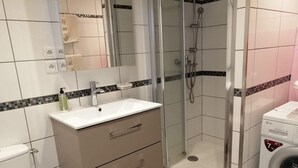 A modern bathroom with a white sink, mirror, and glass-enclosed shower. - T3 in Saint Cyprien, 400m from the beach (Saint-Cyprien Plage)