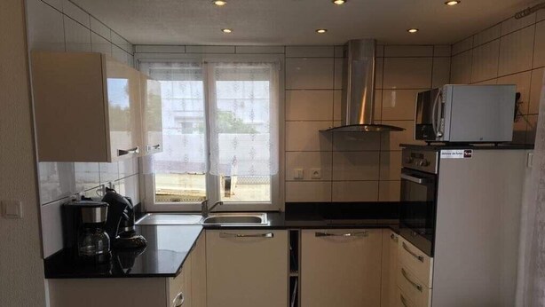 A compact kitchen with white cabinets, a black countertop, a stainless steel range hood, and a microwave on top of the oven. - T3 in Saint Cyprien, 400m from the beach (Saint-Cyprien Plage)