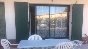 A table with four white chairs, a glass door with green shutters, and a view of buildings through the door. - T3 in Saint Cyprien, 400m from the beach (Saint-Cyprien Plage)