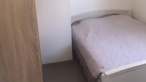 A small, neatly arranged bedroom with a single bed, a wooden door, and a white wall. - T3 in Saint Cyprien, 400m from the beach (Saint-Cyprien Plage)