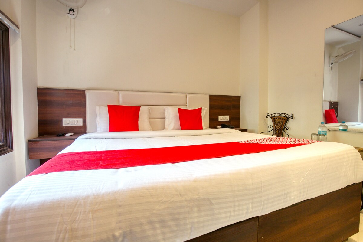 A neatly made bed with white and red bedding, a wooden headboard, and a bedside table with a lamp and a remote control.