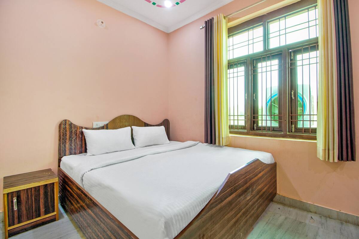 A bedroom with a bed, a nightstand, a window with curtains, and a ceiling light.