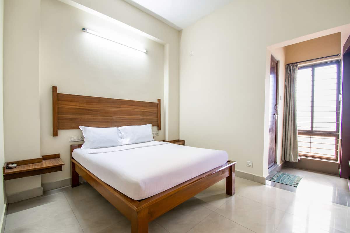 Een verzorgde slaapkamer met een houten bed, wit beddengoed, een nachtkastje en een raam met gordijnen.
