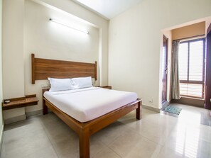 Une chambre à coucher bien rangée, avec un lit en bois, du linge de lit blanc, une table de chevet et une fenêtre avec des rideaux.