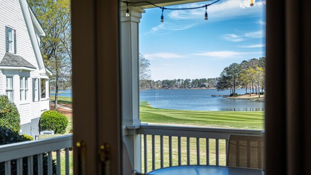 A view from a porch with a table and chairs, overlooking a lake and a golf course.