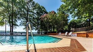 A swimming pool with a metal ladder, surrounded by a brick deck and trees.