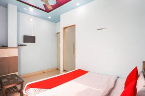 Une chambre d’hôtel avec un lit, un téléviseur fixé au mur, une petite table et une porte donnant sur une autre pièce.