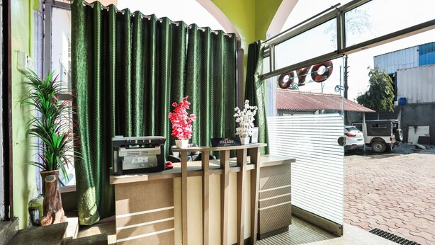 Un mostrador de recepción con un fondo de cortina verde, una planta en maceta y un cartel que dice 'WIZARD'.