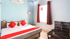 Una habitación de hotel con cama, mesita de noche, una mesa y una ventana con cortinas.