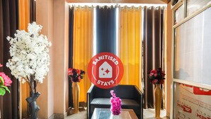 Zona de recepción de hotel con un cartel que dice 'Sanitised Stays', un sofá, una mesa de centro y dos jarrones con flores.