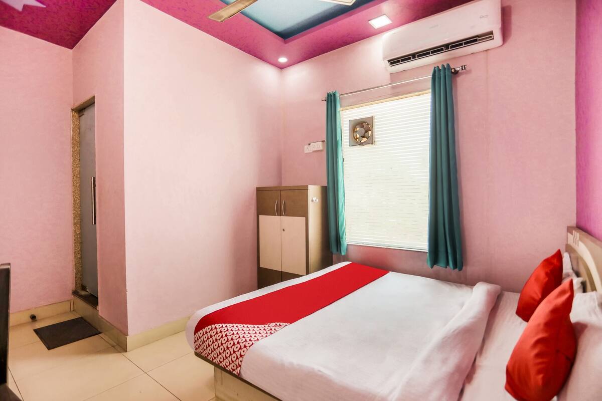 A bedroom with a bed, a wardrobe, a window with curtains, and an air conditioning unit.