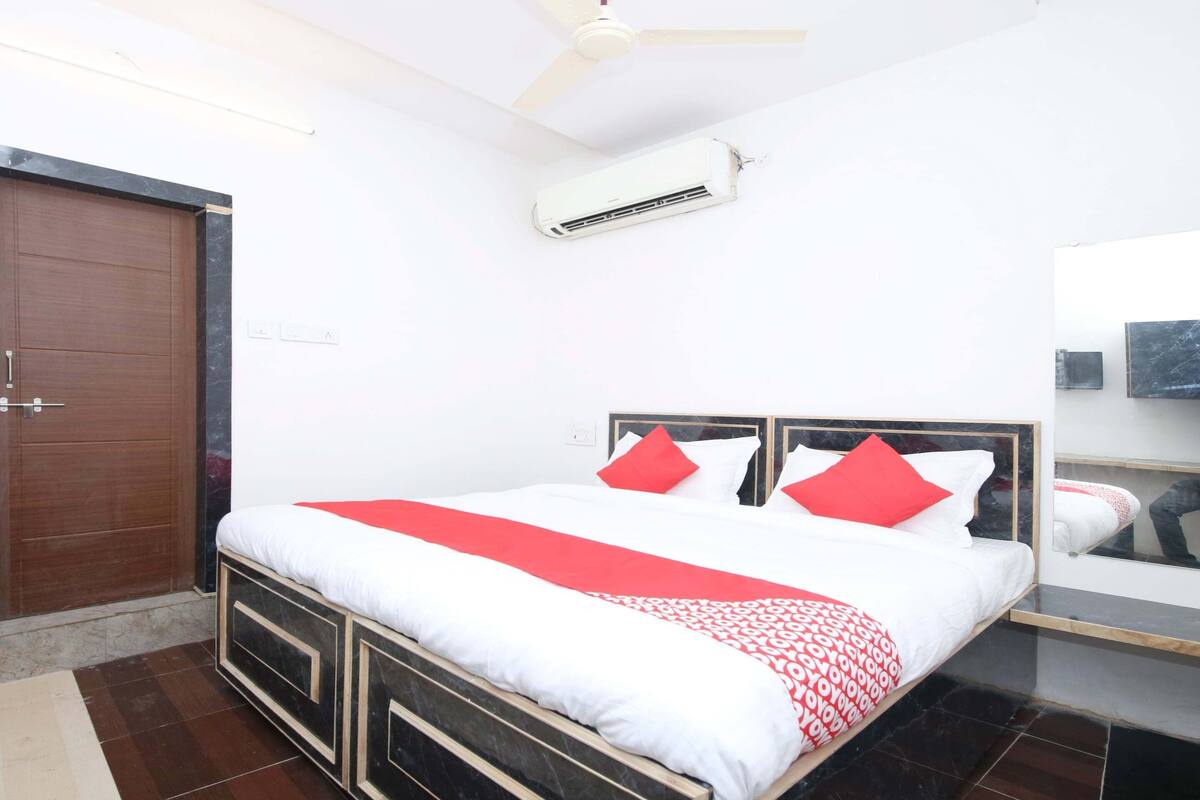 A neatly arranged bedroom with a bed, a ceiling fan, an air conditioning unit, and a wooden door.