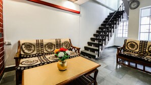 A spacious living area with a wooden table, two sofas with patterned cushions, a vase of flowers, and a staircase leading to an upper floor.