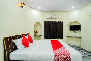 A hotel room with a bed, a TV, a window with curtains, and an air conditioning unit. - OYO 30000 Hotel Panghat (Kota)