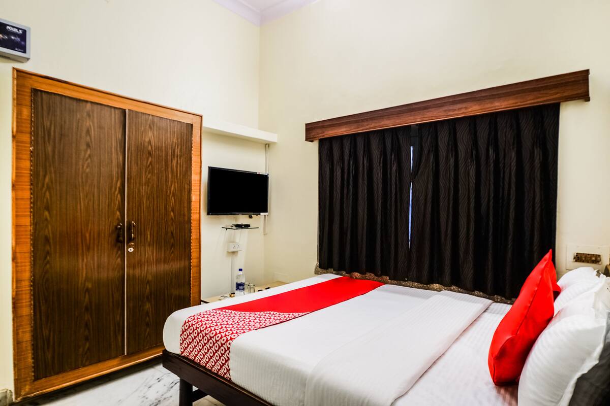 Quarto de hotel com cama, guarda-roupa, televisão e janela com cortinas.