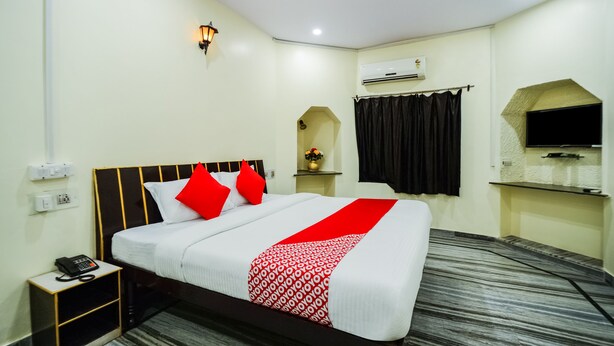 A hotel room with a bed, a nightstand, a telephone, an air conditioning unit, and a wall-mounted TV.