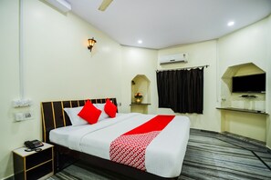 Habitación de hotel con cama, mesita de noche, teléfono, unidad de aire acondicionado y televisor montado en la pared.