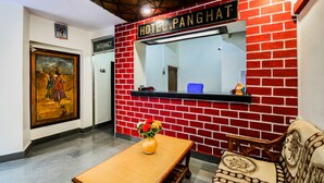 A reception area with a red brick wall, a reception desk, a wooden bench, and a vase with flowers.