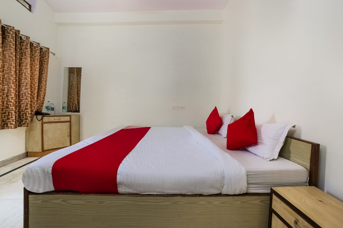 A neatly made bed with a red and white bedspread, a wooden nightstand, and a small wooden cabinet.