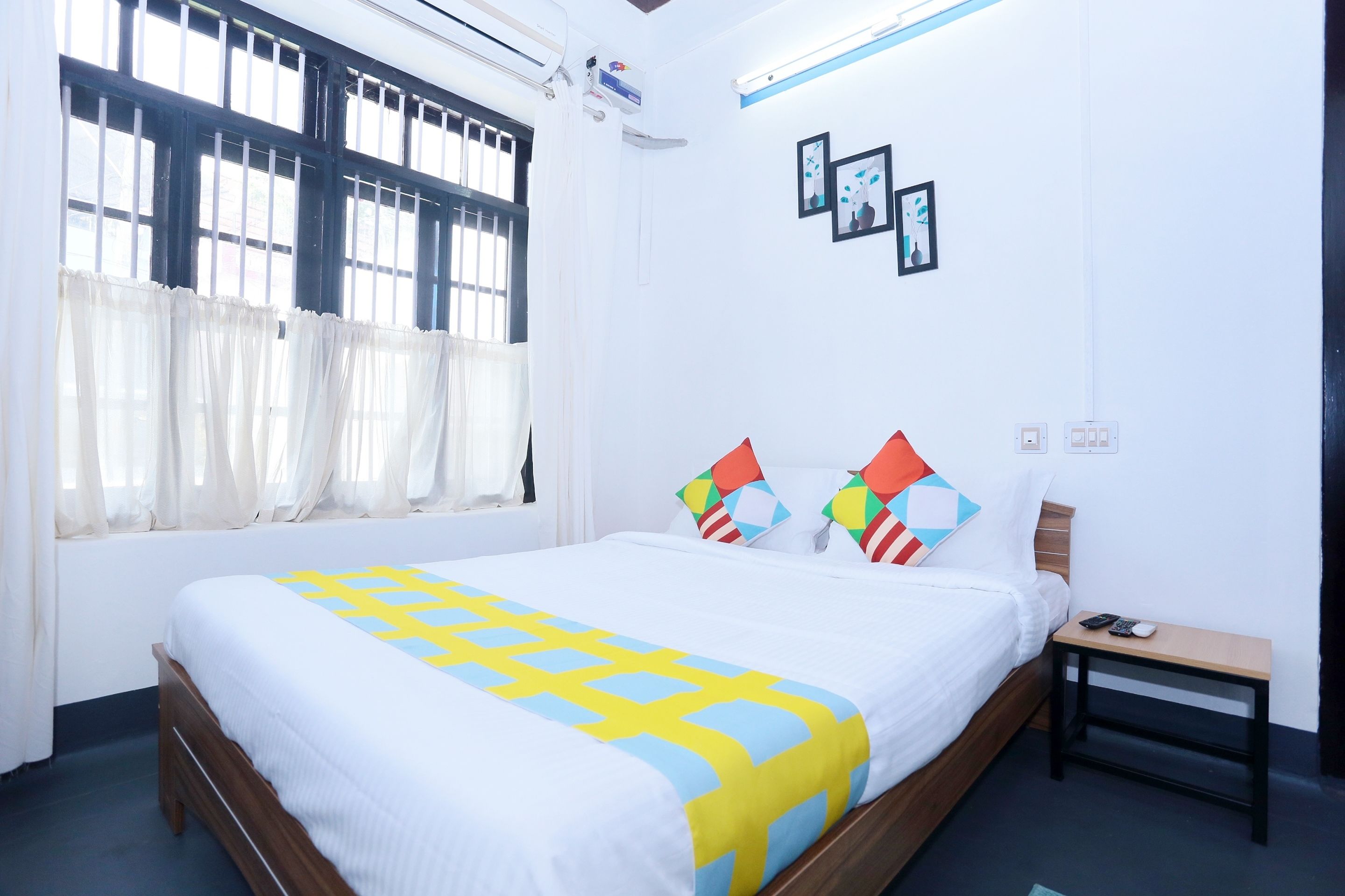 A neatly made bed with a patterned bedspread, a bedside table with a phone and remote, and a window with curtains.