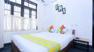 A neatly made bed with a patterned bedspread, a bedside table with a phone and remote, and a window with curtains.