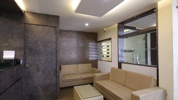 A modern living room with a sofa, a coffee table, and a TV. There is a glass door with a sign that reads "RESTAURANT". - OYO 28093 Royal Sand (Mysore)