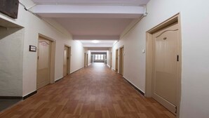 A long, narrow hallway with wooden flooring and beige doors, leading to a bright room at the end. - OYO 28093 Royal Sand (Mysore)