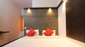 A modern hotel room with a large bed, two red pillows, and a dark headboard. - OYO 28093 Royal Sand (Mysore)