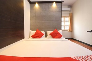 A hotel room with a bed, two red pillows, a window with curtains, and an air conditioning unit. - OYO 28093 Royal Sand (Mysore)