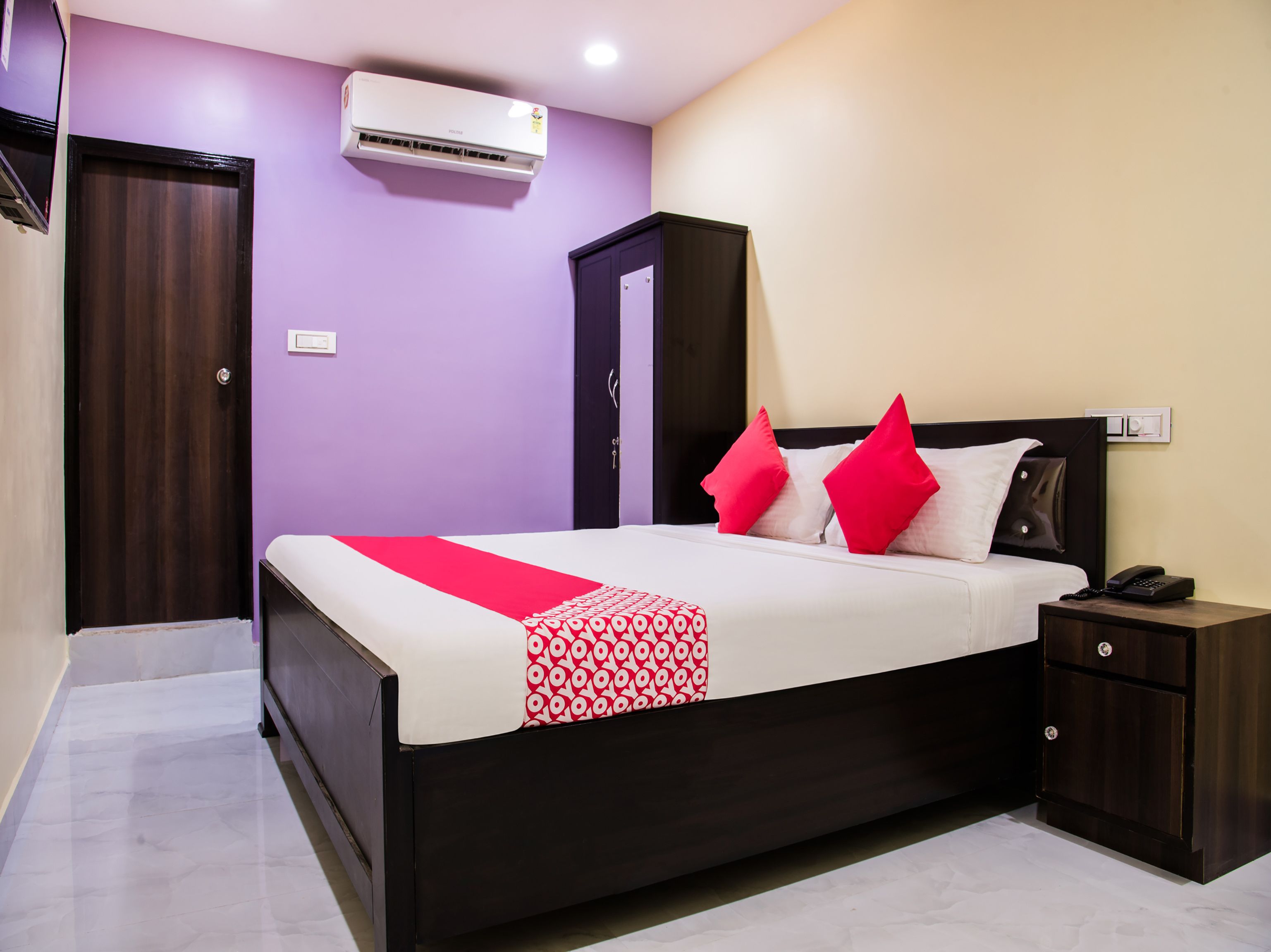 A bedroom with a bed, a nightstand, a wardrobe, and an air conditioning unit.