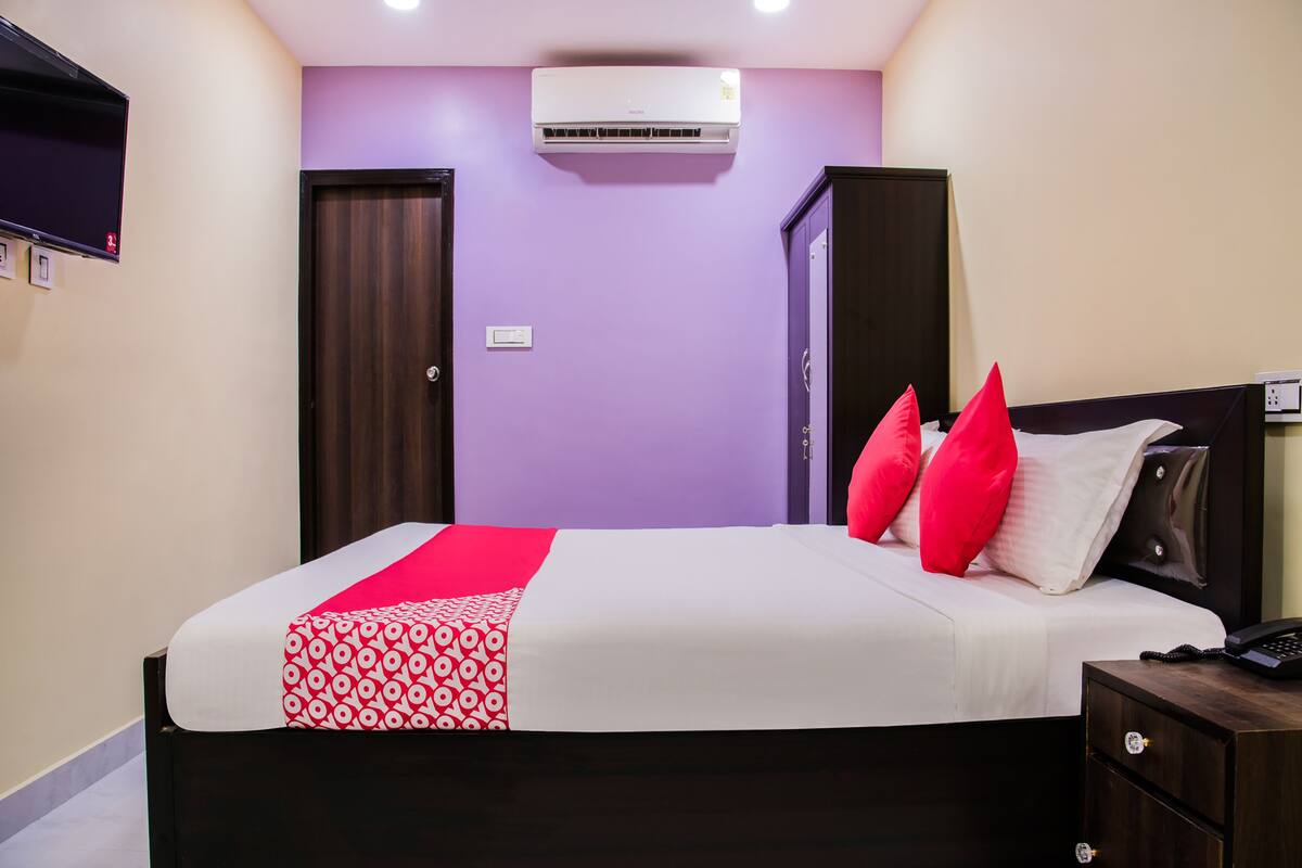 Un dormitorio ordenado con cama, mesitas de noche, un equipo de aire acondicionado y un televisor montado en la pared.