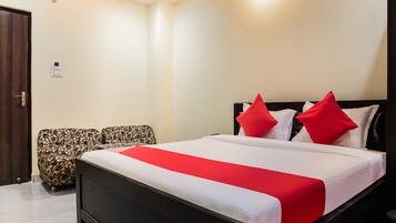 A neatly arranged bedroom with a large bed, two patterned armchairs, a wooden door, and a light-colored wall.
