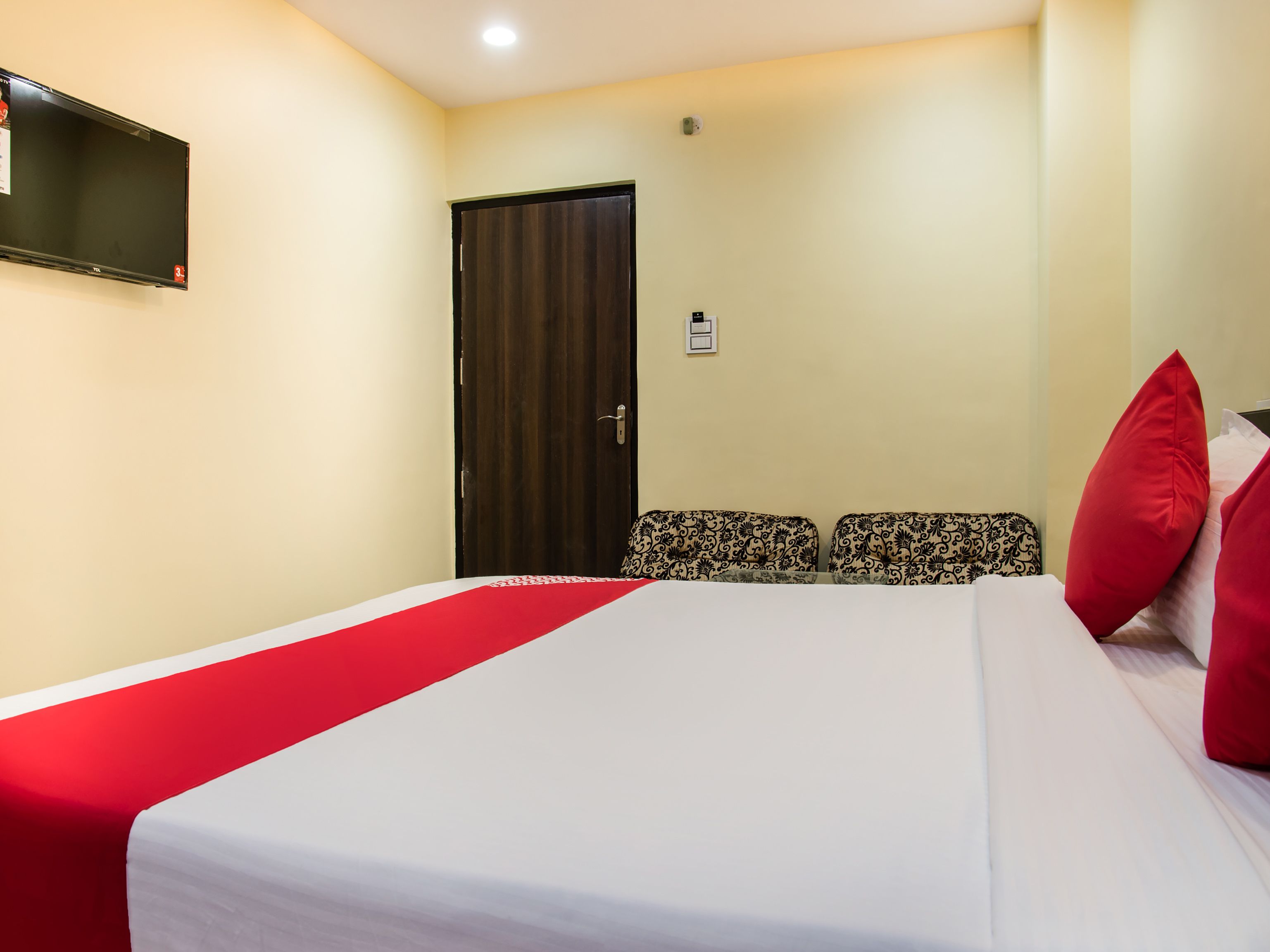 A hotel room with a bed, a TV mounted on the wall, a door, and a small table with chairs.