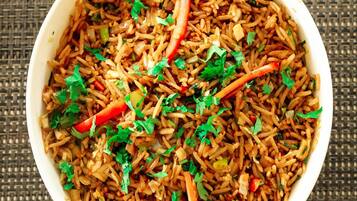 Un tazón de arroz frito con verduras y hierbas.