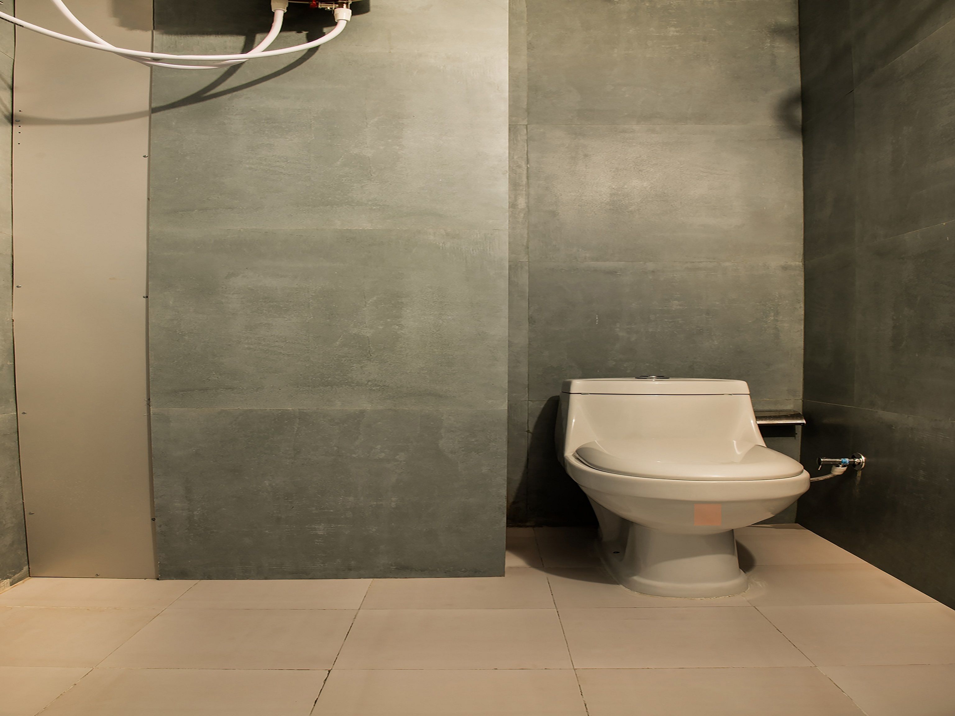 A modern bathroom with a toilet, grey tiled walls, and a tiled floor.