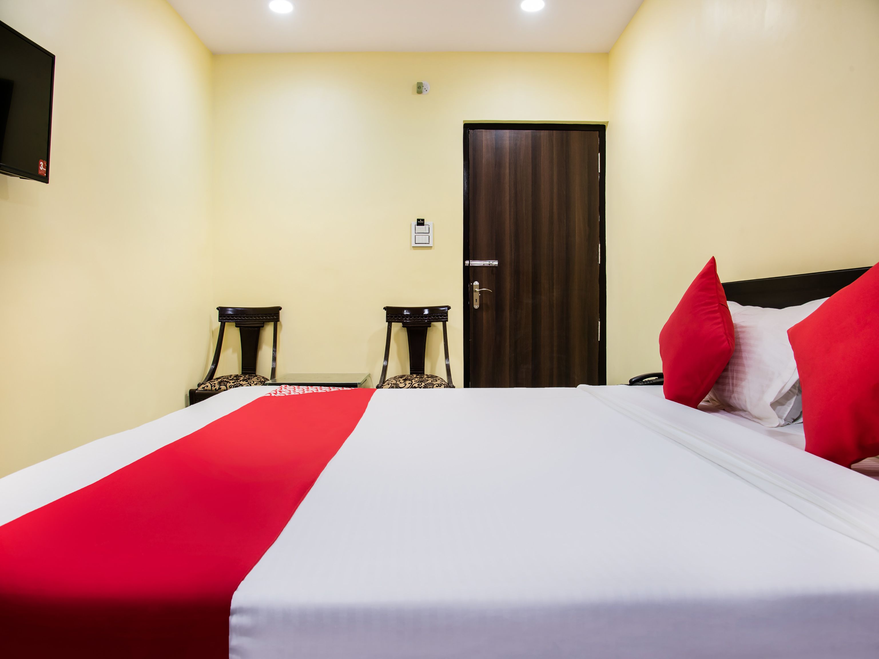 A hotel room with a bed, two bedside tables, a door, and a wall-mounted TV.