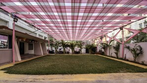 An outdoor courtyard with a checkered canopy, a grassy area, and several parked motorcycles. - OYO Flagship 23420 Patliputra Heritage Guest House (Patna)